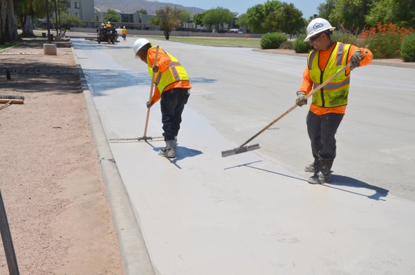 Two workers apply liquid material to pavement.