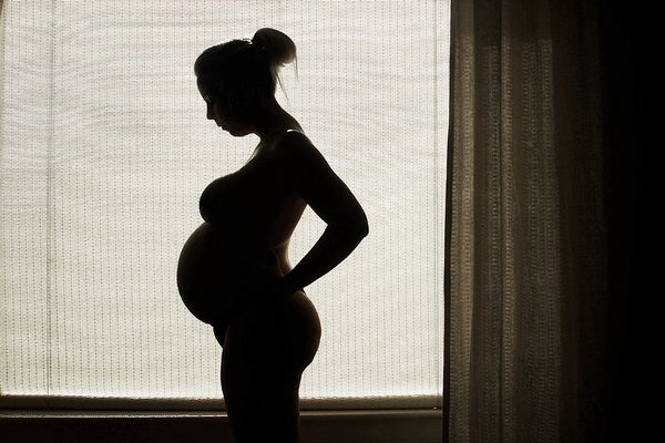 Silhouette of pregnant person in front window with shade drawn.