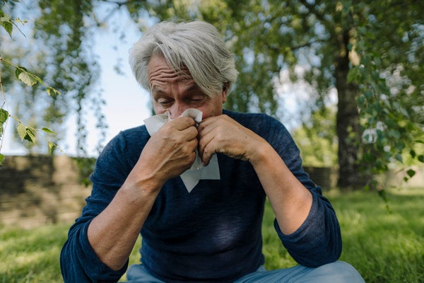Senior man blowing nose while sitting in field