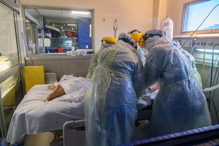 Health workers huddle over a patient's hospital bed.