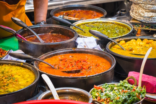 A street vendor with several large pots containing various Indian curry dishes