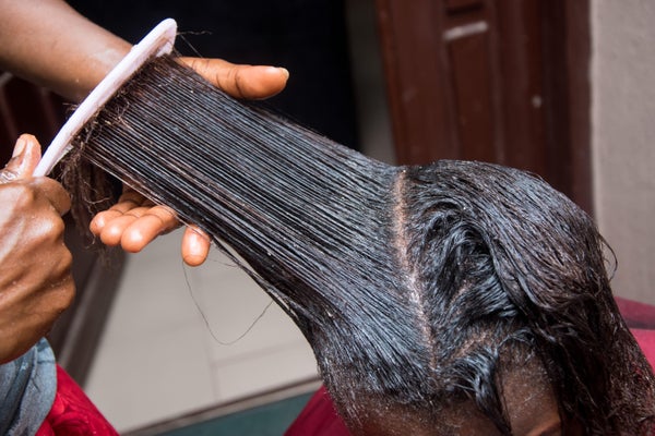 Hairdresser relaxing the hair on an african woman head and also using comb to stretch and apply the relaxer cream through the hair