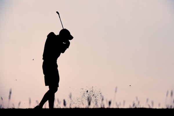 Silhouette of golf player taking a shot at sunset.