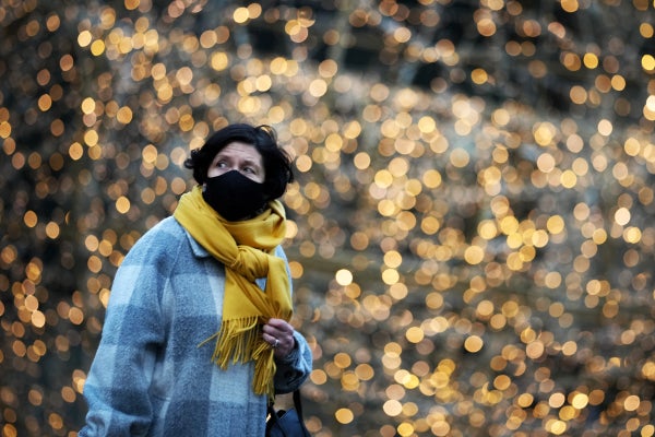 A woman walks in front of sparkly holiday lights.