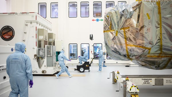 Engineers in blue cleanroom suits moving a crate with the covered Hope probe