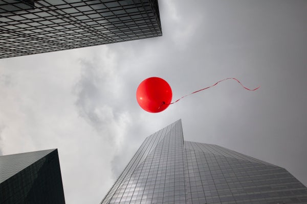 A red balloon floats among skyscrapers.