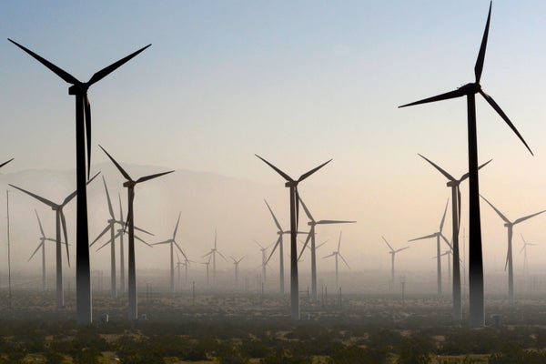 Tall wind turbines generate electricity as a dust storm blows through the area at dusk.