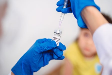 Doctor in protective gloves filling injection syringe with COVID-19 vaccine and ready to give to a child.
