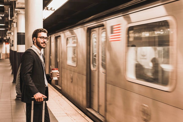 Young businessman waiting at subway station platform holding coffee cup