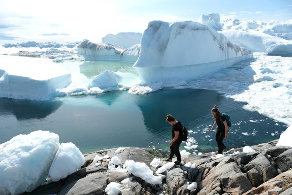 2 visitors walk among free-floating ice in Greenland.