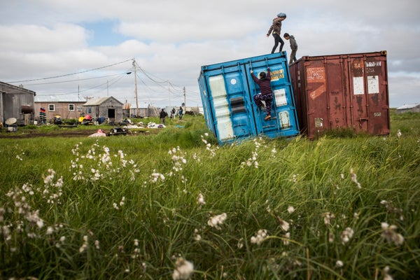 Yupik children climbing on containers on grassland in front of their village