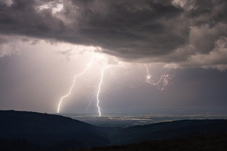 Aerial view of two powerful lightning strikes in the distance stretching from the ground do overhead storm clouds