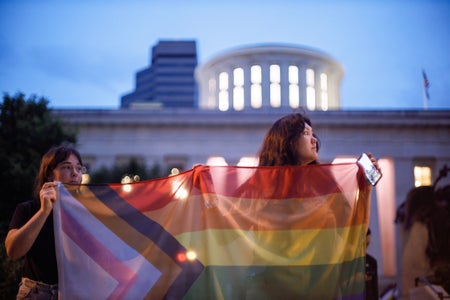 Two young people hold a pride flag at a nighttime rally.