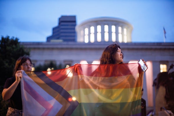 Two young people hold a pride flag at a nighttime rally.