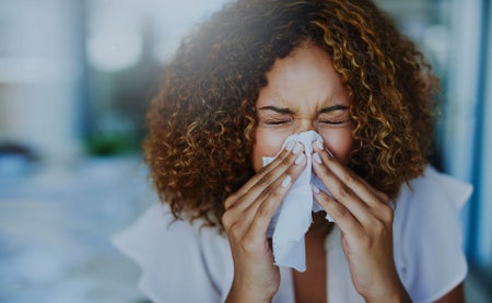 Woman with curly hair blowing nose w/ tissue