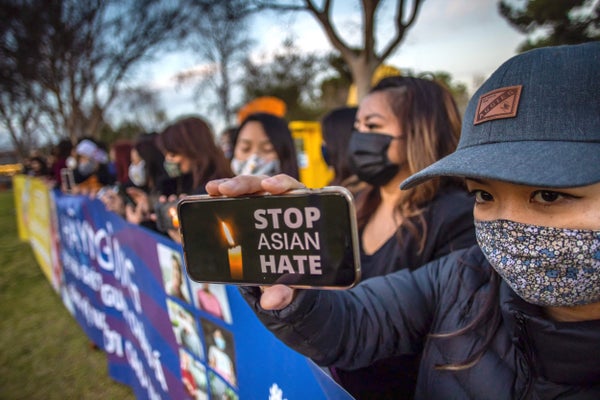 Women protesting anti-Asian racism; one holds up a phone with an image of a candle and the words "Stop Asian Hate".