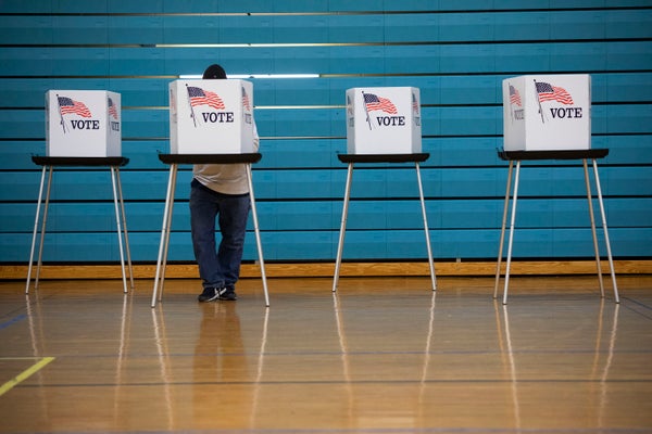 A man standing behind a voting booth w/ blue background