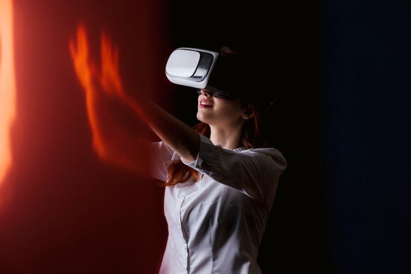 Young woman gesturing while using VR glasses over black background