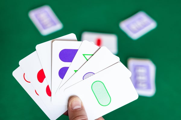 Thumb holding 6 white playing cards with symbols with green table backround.