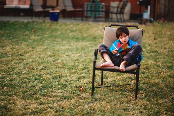 A small child sits barefoot on chair in yard reading a book in Spring