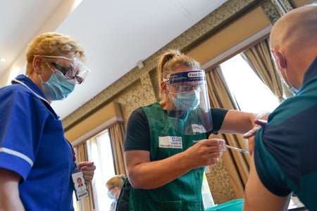 A man receives the Covid vaccine attended by 2 women healthcare workers.