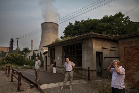 Men standing on porches in front of coal plant with billowing smoke.