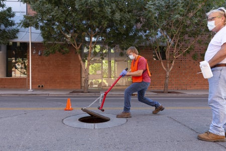 Masked student lifts manhole cover on college campus