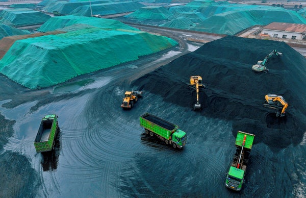 Aerial view of green trucks and machinery during coal being unloaded.