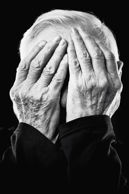 Older man covering his face with his hands.