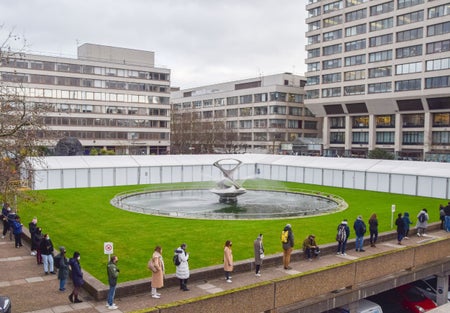 Socially distanced line of people wait outside hospital.