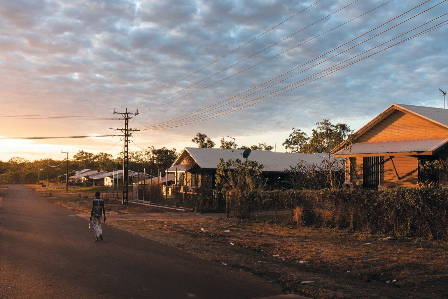 Early morning scene showing person walking on street with two buildings in foreground and some other buildings in the background.