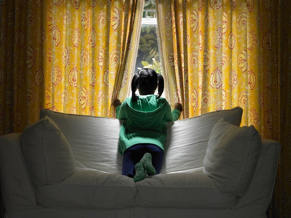 Girl kneeling on sofa, looking out window, rear view