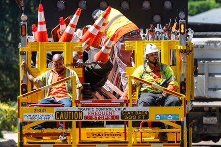 LA County road crew workers sit on the back of a utility truck, visibly exhausted from heat