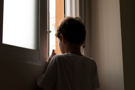 Rear View Of Boy Looking Through Window At Home