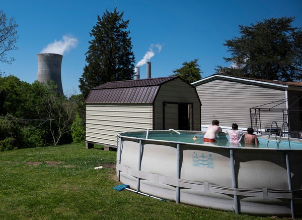 Kids take a break in a swimming pool at their grandparents home as steam rises from coal power plant