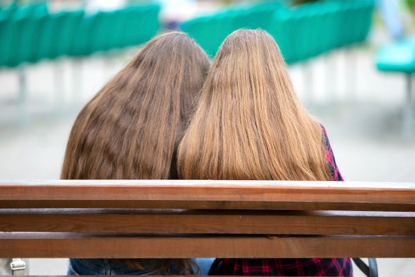 Two girls with long hair are sitting on a bench.