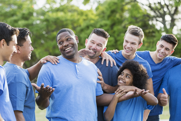 A group of men standing together outdoors in the park wearing blue shirts. One man is the center of attention.