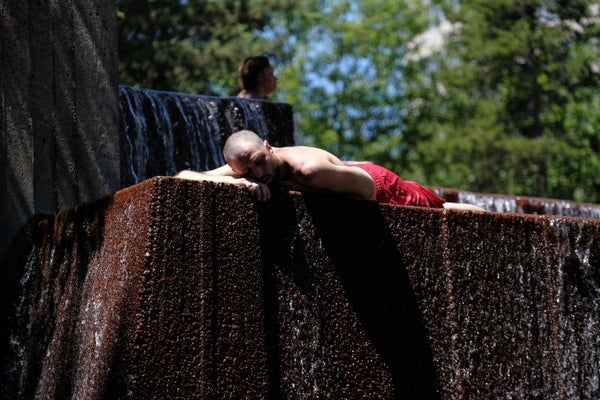A man in swimtrunks lays on a public fountain