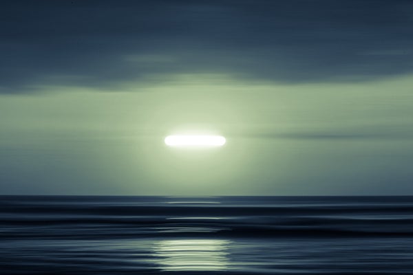 A disk-shaped, brilliant light shines in the sky over the ocean.