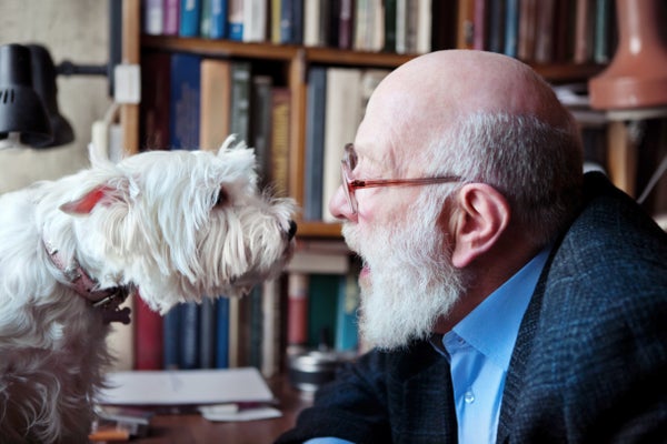 Senior man with glasses talking to small white dog, face to face