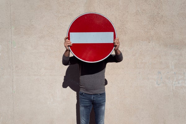 Adult man standing in front of wall holding a no entry sign in front of his face