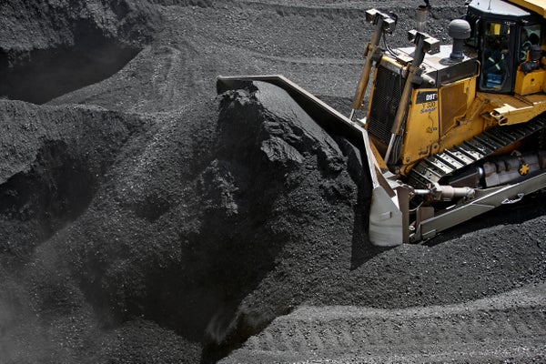 A yellow bulldozer plows a massive pile of coal.