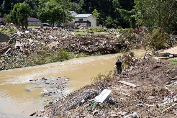 Person walks by flooded creek surrounded by rubble