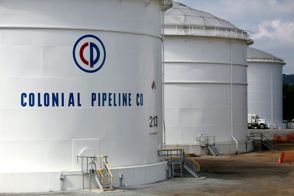 Three large white storage tanks and part of a truck are visible. "Colonial Pipeline Co" is painted on one of the tanks.