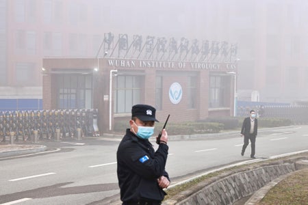 Security officer listening to communication device stands outside Wuhan Institute of Virology building.