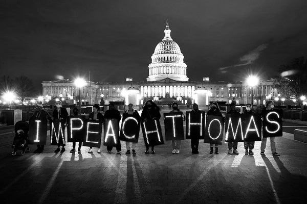 Night view showing group of people holing signs with individual letters that together, spell "IMPEACH THOMAS"