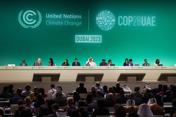 Sultan Ahmed Al Jaber (C), President of the UNFCCC COP28 Climate Conference and other deligates sitting in front of green backdrop with UN signage, Cop 28 signage and Dubai 2023 in front of audience.