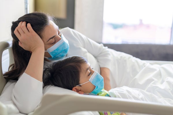 Tired sleeping mother lying on the hospital bed with sick kid wearing protective face mask