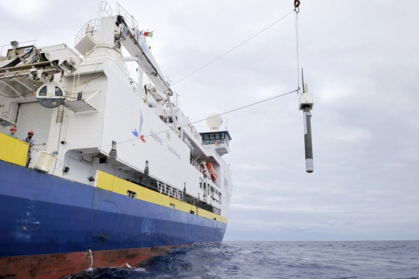 A large floating temperature device is being lower into the ocean from a large ship.