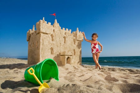 Young girl next to over sized sand castle with green bucket in front